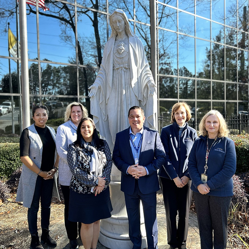 Office of Mission Advancement Staff standing before a statue of our lady outside the chancery.